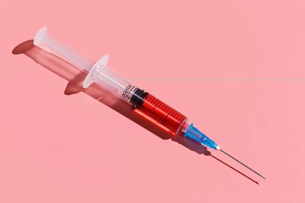 Siringa con vaccino rosso su sfondo rosa. Primo piano piatto lay — Foto Stock