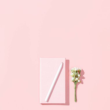 Boş pembe defter, beyaz kalem, pembe arka planda çiçek dalı olan minimalist kart modeli. Bahar feminen blog yazarı konsepti. Düz konum, kare resim, üst görünüm, boşluk kopyala