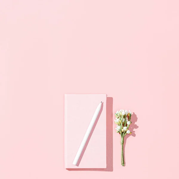 Maqueta de tarjeta minimalista con cuaderno rosa vacío, bolígrafo blanco, rama de flor sobre fondo rosa. Concepto de bloguera femenina de primavera. Colocación plana, imagen cuadrada, vista superior, espacio para copiar — Foto de Stock