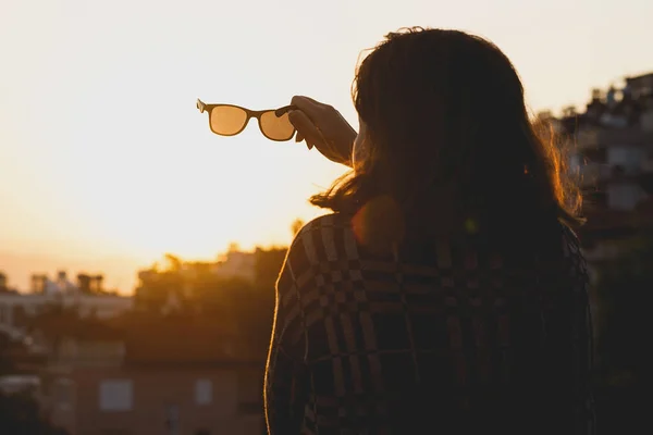 Eine junge Frau trifft den Sonnenaufgang auf dem Dach und hält eine Sonnenbrille in der Hand — Stockfoto