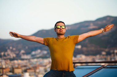 Çatıda gözlüklü yakışıklı bir adam şafağın, temiz havanın ve özgürlüğün tadını çıkarıyor.