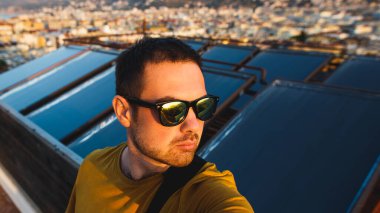 Çatıda gözlüklü yakışıklı bir adam şafağın, temiz havanın ve özgürlüğün tadını çıkarıyor.