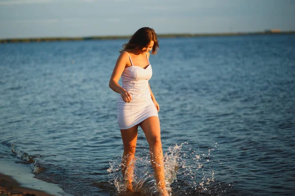 Mujer sexy juguetona divirtiéndose en la playa al atardecer. Joven mujer bronceada alegre salpicando sus piernas en agua tibia. Concepto sin preocupaciones de verano — Foto de Stock