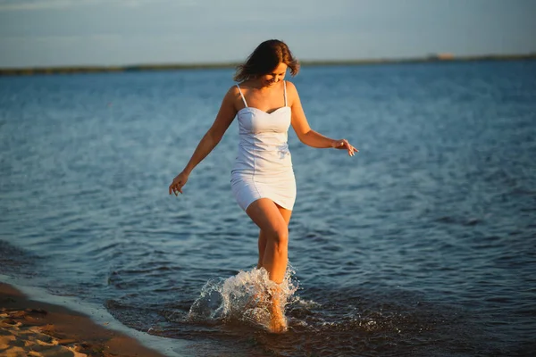 Playful sexy woman having fun on the beach on the sunset. Веселая молодая загорелая женщина, брызгающая ногами в теплой воде. Концепция летней кареты — стоковое фото