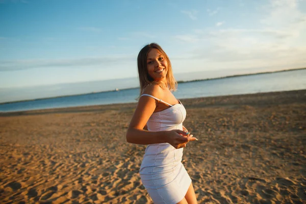 Mujer sexy juguetona divirtiéndose en la playa al atardecer. Joven alegre con forma perfecta en vestido sexy —  Fotos de Stock