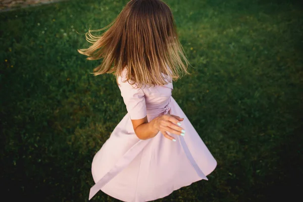 Όμορφο χαρούμενο κορίτσι πέφτει πάνω σε ένα χορό στο πράσινο γρασίδι. Ένα λεπτό ροζ φόρεμα φτερουγίζει όμορφα. Δυναμικό πορτρέτο από ψηλά — Φωτογραφία Αρχείου