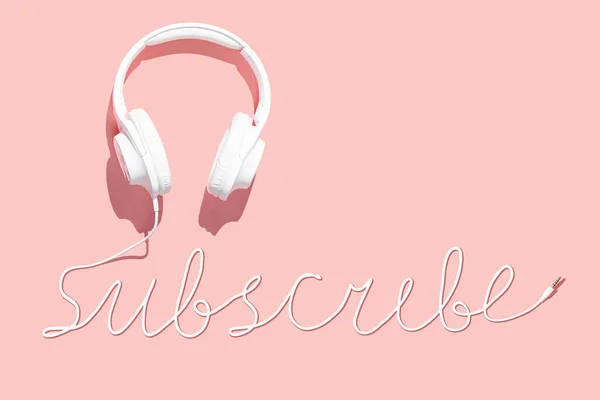 White headphones and a word subscribe from the cord on a pink background. Stay home concept, trendy flat lay.