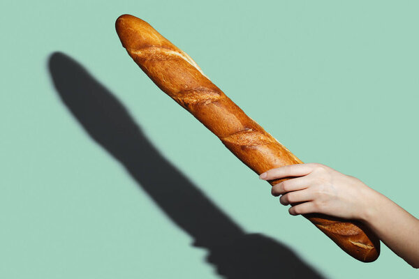 Female hands hold a bread loaf on green background. Flat lay, direct light