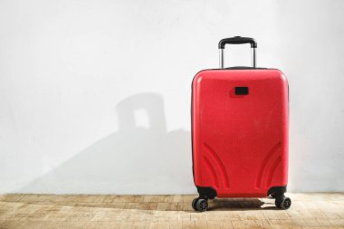Red suitcase against the background of a light wall in the room. Stay home, travel concept. Copy space clipart