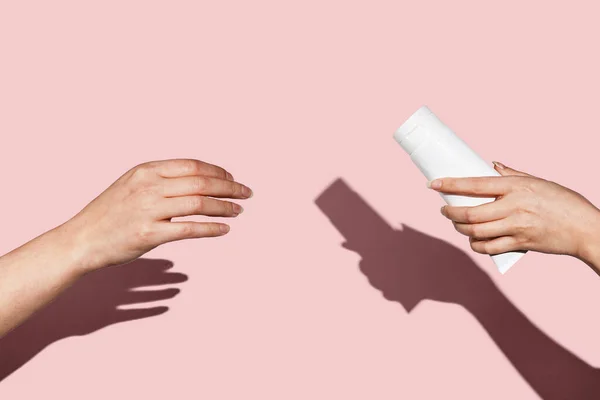 Женские руки давая девушкам руку белая тюбик крема на розовом фоне прямой свет — стоковое фото