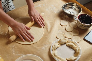 Kadın elleri hamuru un içinde yuvarlıyor. Mutfağında merdane var.