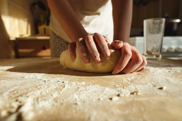Женские руки месят тесто на столе под теплым солнцем — стоковое фото