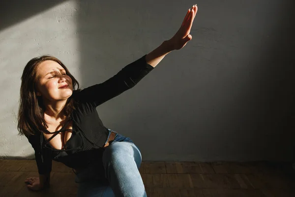 Donna che si nasconde dal sole nella stanza domestica. Luce dal sole sul viso e ombra dalle mani. Lei indossa sul corpo nero e jeans — Foto Stock