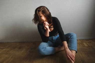 Güneşli bir günde odanın zemininde poz veren çekici bir kadın. Koyu yakalı ve kot pantolonlu siyah bir vücudu vardı.