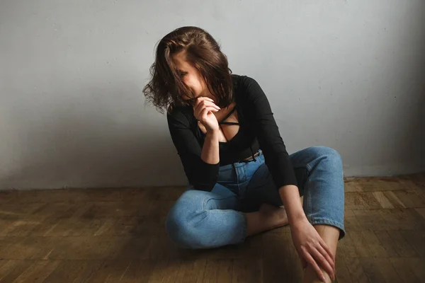 Mulher atraente posando no chão da sala em dia ensolarado. Vestida de corpo negro com decote profundo e jeans azuis — Fotografia de Stock