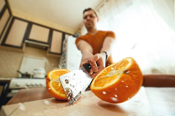 Hombre cortando jugosa naranja por la mitad con salpicaduras en la cocina. Primer plano de gran angular. Bloqueo creativo — Foto de Stock