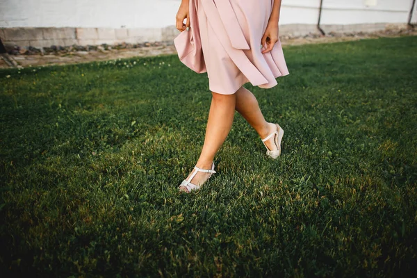 Pies femeninos en sandalias. Pasos sobre la hierba Una chica en un sarafán rosa — Foto de Stock