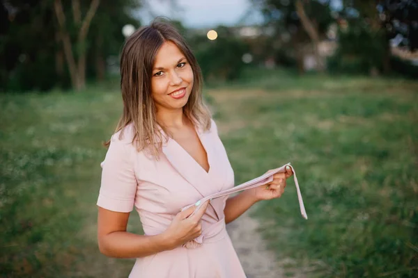 Giovane donna giocosa in abito estivo rosa gode di una passeggiata nel parco primaverile la sera — Foto Stock