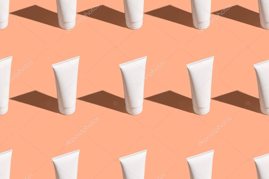 White cream tubes on lifht orange table. Care about face, hands, legs and body skin. Women beauty products. Cosmetic regular pattern. Empty place for logo on bottles. Hard light directly above flat