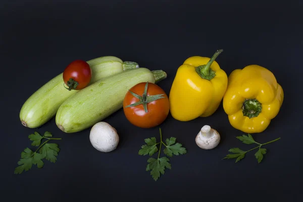 Yellow peppers with zucchini and tomatoes on a dark background. Composition from different vegetables on a dark background. White mushrooms with peppers and tomatoes.
