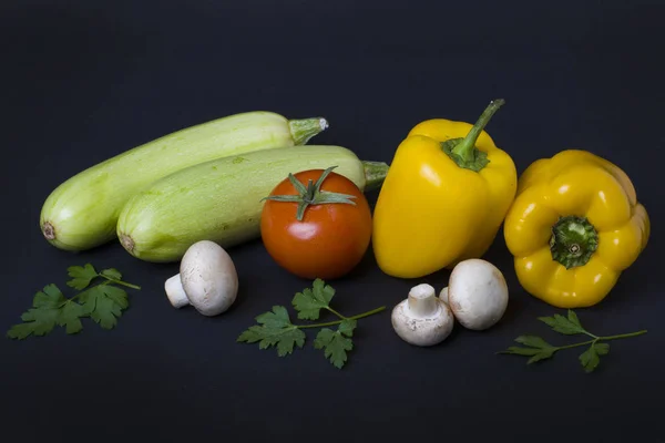 Yellow peppers with zucchini and tomatoes on a dark background. Composition from different vegetables on a dark background. White mushrooms with peppers and tomatoes.