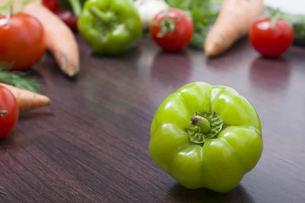 The green peppers on a table on the background of vegetables. Fresh tomatoes and peppers on a wooden brown table