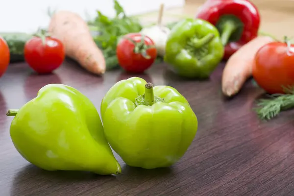 Red tomatoes and green peppers on a table on the background of vegetables. Fresh tomatoes and peppers on a wooden brown table