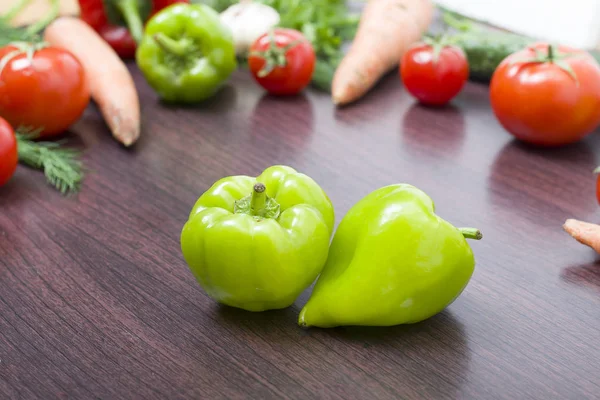 Red tomatoes and green peppers on a table on the background of vegetables. Fresh tomatoes and peppers on a wooden brown table