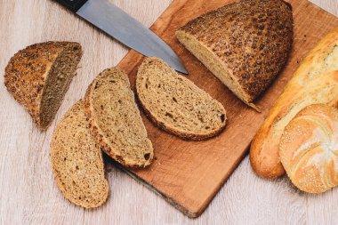 Ahşap arka planda farklı türler. Tahtada bir bıçak ve masada farklı çörekler. Tahtada çıtır ekmek.