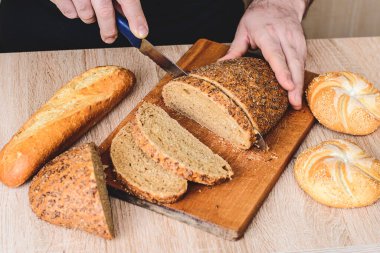 Bıçaklı bir adam tahta bir tahtada ekmek keser. Fransız ekmeği. Ahşap arka planda farklı türler.