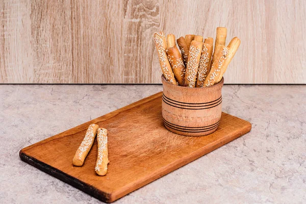 Crispy bread sticks with sesame seeds and bran bread on a wooden board.