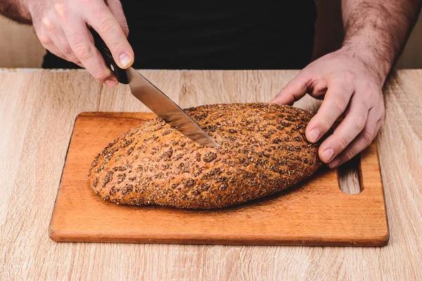 A man with a knife cuts bread on a wooden board.