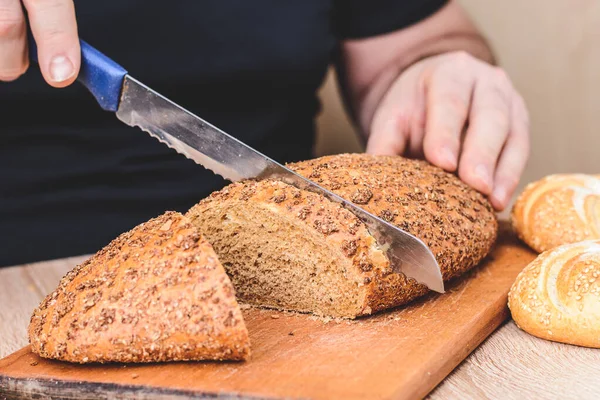 Bıçaklı bir adam tahta bir tahtada ekmek keser. Fransız ekmeği. Ahşap arka planda farklı türler.