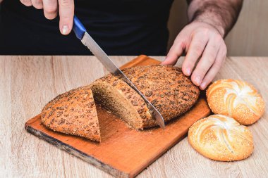 Bıçaklı bir adam tahta bir tahtada ekmek keser. Fransız ekmeği. Ahşap arka planda farklı türler.