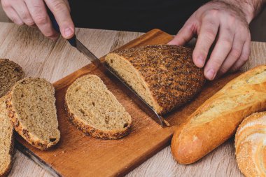 Bıçaklı bir adam tahta bir tahtada ekmek keser. Fransız ekmeği. Ahşap arka planda farklı türler.