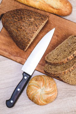 Ahşap arka planda farklı türler. Tahtada bir bıçak ve masada farklı çörekler. Tahtada çıtır ekmek.