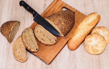 Ahşap arka planda farklı türler. Tahtada bir bıçak ve masada farklı çörekler. Tahtada çıtır ekmek.