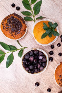 Çikolatalı kek ve fındıklı kek, arka planda ev yapımı fırın. Ahşap bir masada yaban mersinli kek. Tahtada taze böğürtlen ve tatlı börek var..