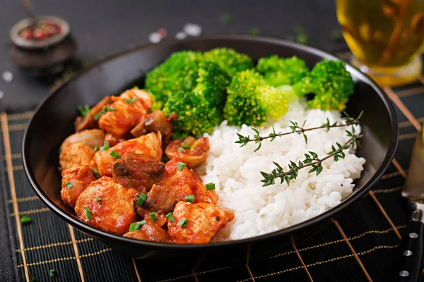 Pieces of chicken fillet with mushrooms stewed in tomato sauce and boiled broccoli with rice in wok