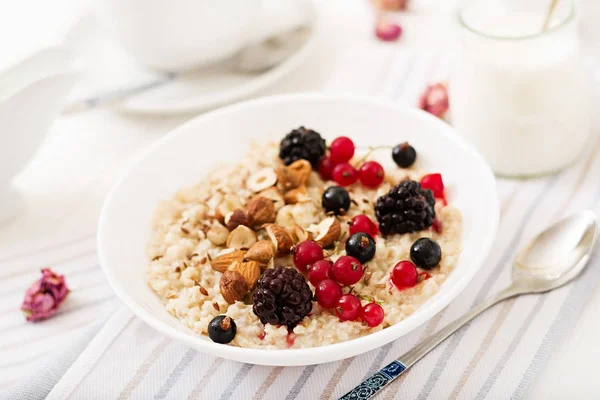Tasty oatmeal porridge with berries and flax seeds with nuts in bowl, healthy breakfast concept