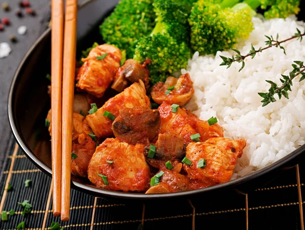 Pieces of chicken fillet with mushrooms stewed in tomato sauce and boiled broccoli with rice in wok
