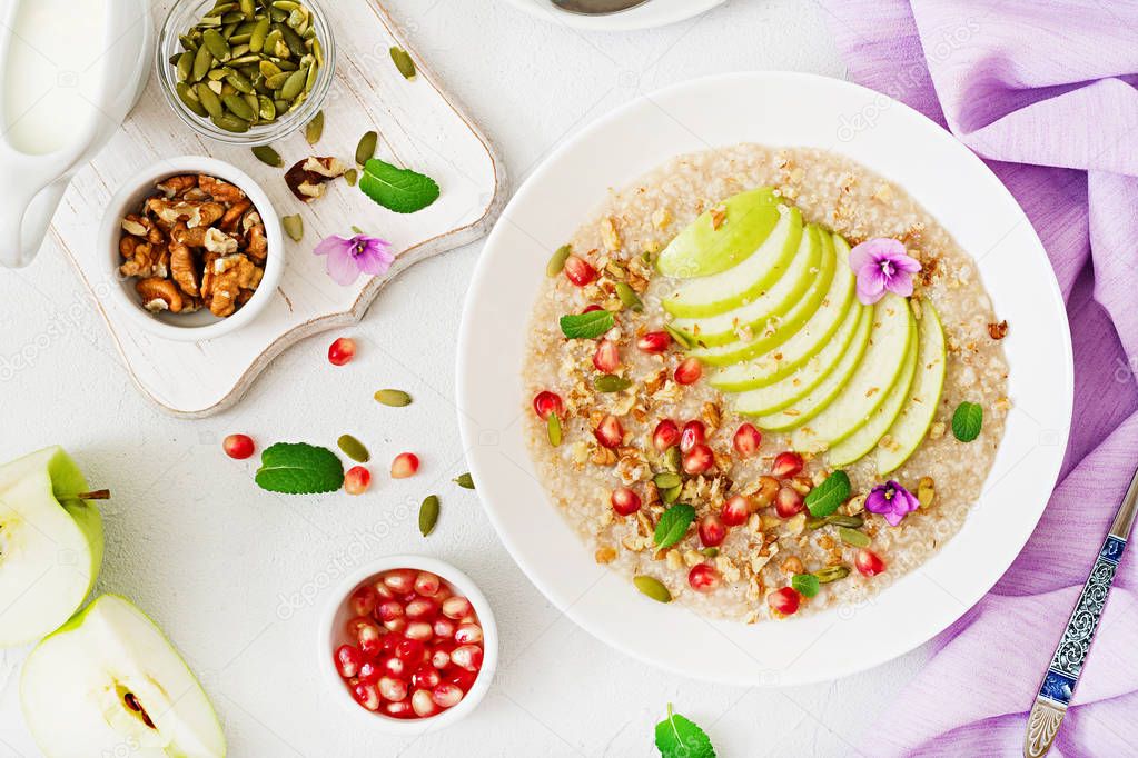 Tasty and healthy oatmeal porridge with apple slices and pomegranate with nuts in bowl