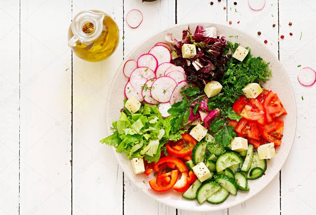 Mix salad from fresh vegetables and greens herbs in white bowl on wooden table 