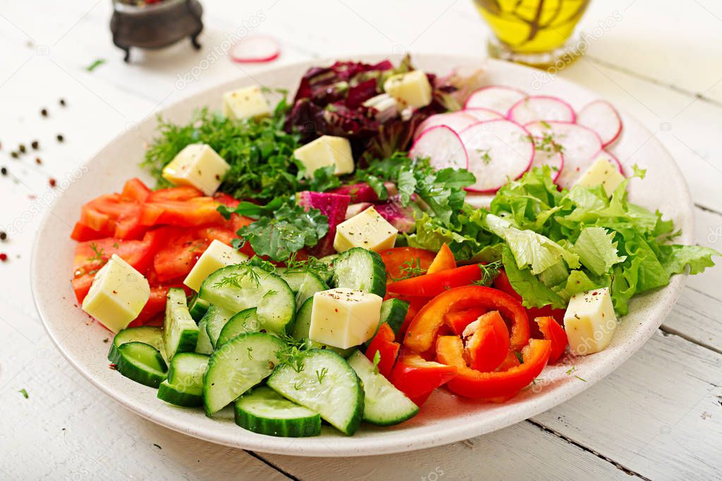 Mix salad from fresh vegetables and greens herbs in white bowl on wooden table 