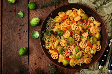 Vejetaryen sebze makarna Rocchetti Brüksel lahanası, domates, patlıcan ve kırmızı biber ahşap masa üzerinde kahverengi kase