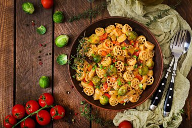 Vejetaryen sebze makarna Rocchetti Brüksel lahanası, domates, patlıcan ve kırmızı biber ahşap masa üzerinde kahverengi kase