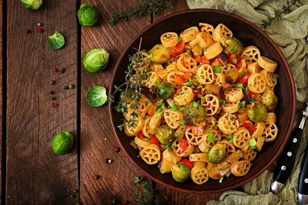 Vejetaryen sebze makarna Rocchetti Brüksel lahanası, domates, patlıcan ve kırmızı biber ahşap masa üzerinde kahverengi kase