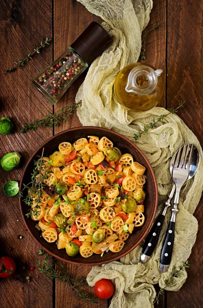 Vejetaryen sebze makarna Rocchetti Brüksel lahanası, domates, patlıcan ve kırmızı biber ahşap masa üzerinde kahverengi kase
