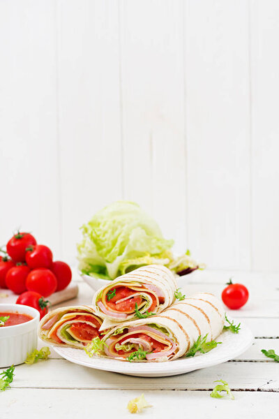 Tortilla wrap with ham, cheese and tomatoes on a white wooden background