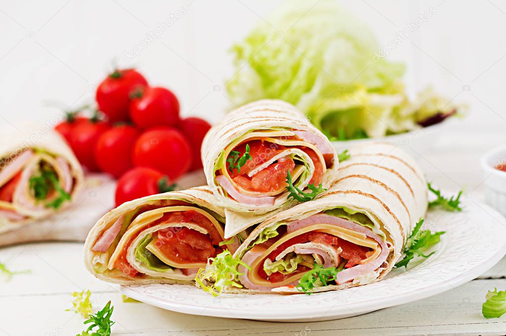 Tortilla wrap with ham, cheese and tomatoes on a white wooden background